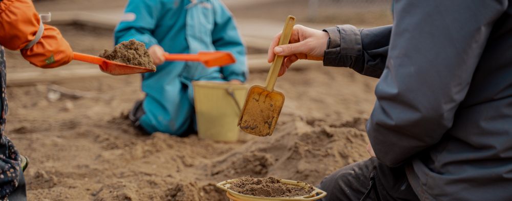 Barnehagebarn som graver med spader i sandkassa